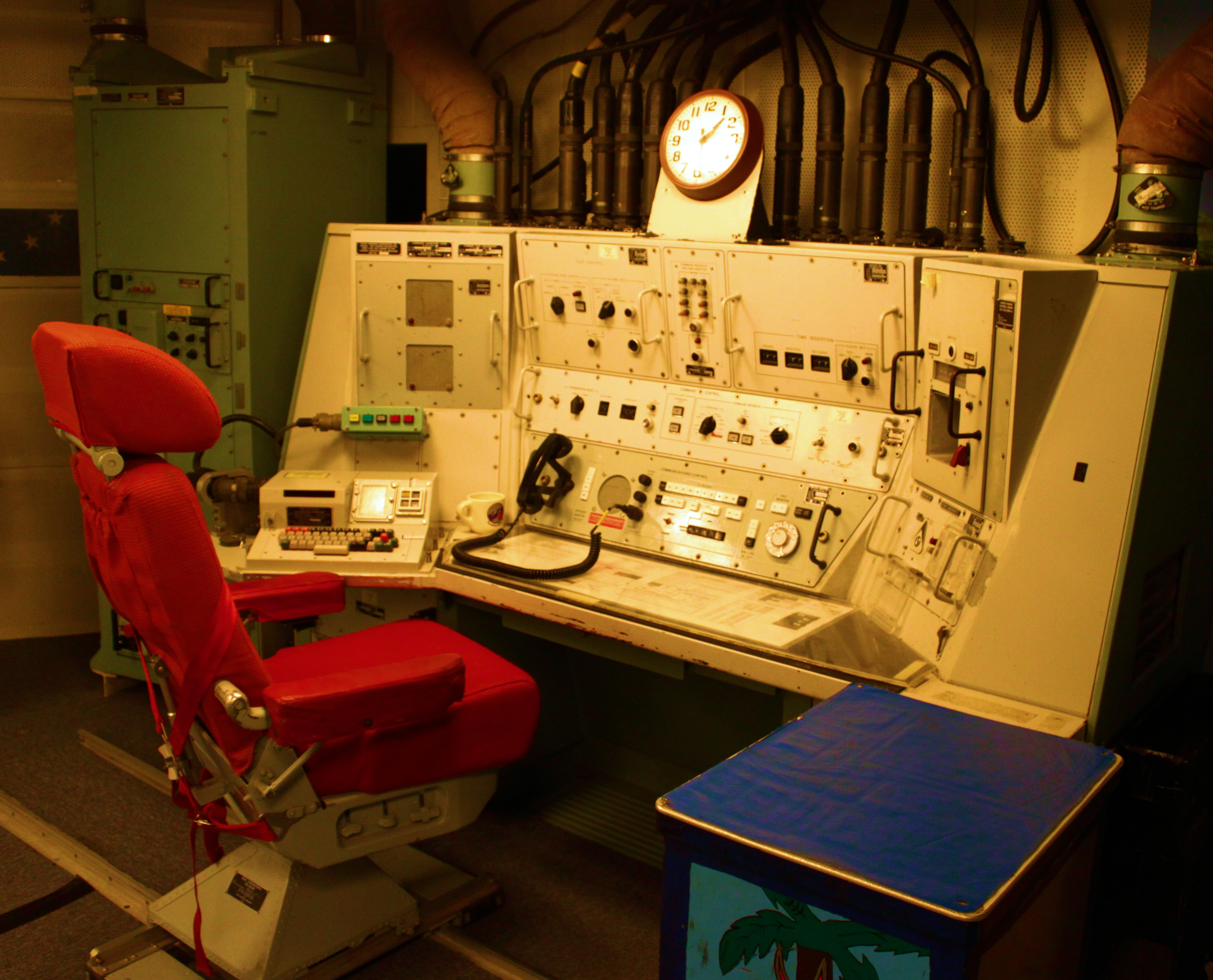 Interior of a Minuteman ICBM launch control capsule, U.S. Air Force public domain archive photograph. Red operator's chair, control consoles with rows of switches, indicator lights, and dials, large analog clock on the back wall. Echo Flight, Malmstrom Air Force Base, March 1967.