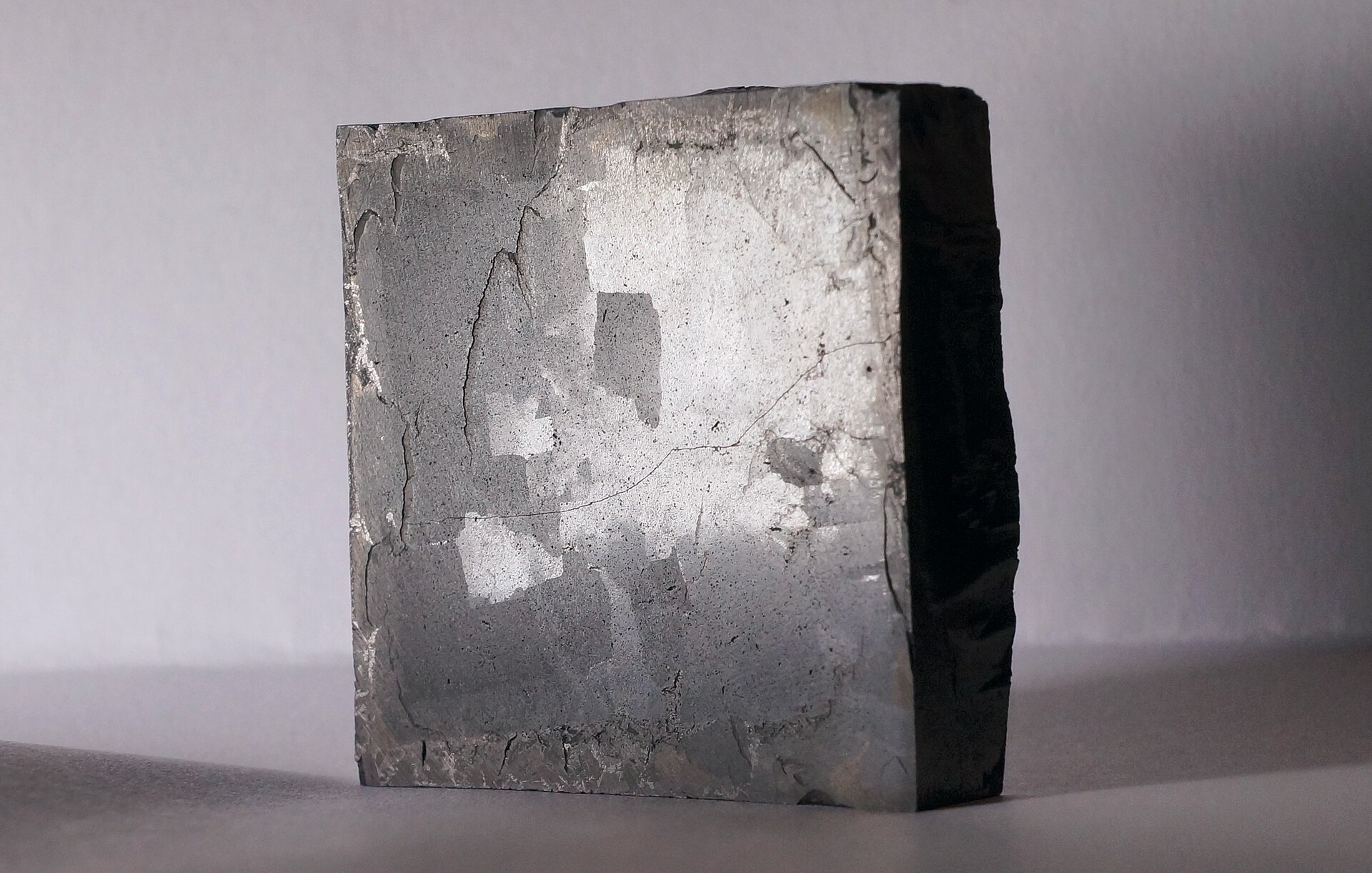 A small dark ceramic YBCO (yttrium barium copper oxide) high-temperature superconductor specimen on a neutral grey surface, photographed in a clean documentary style.