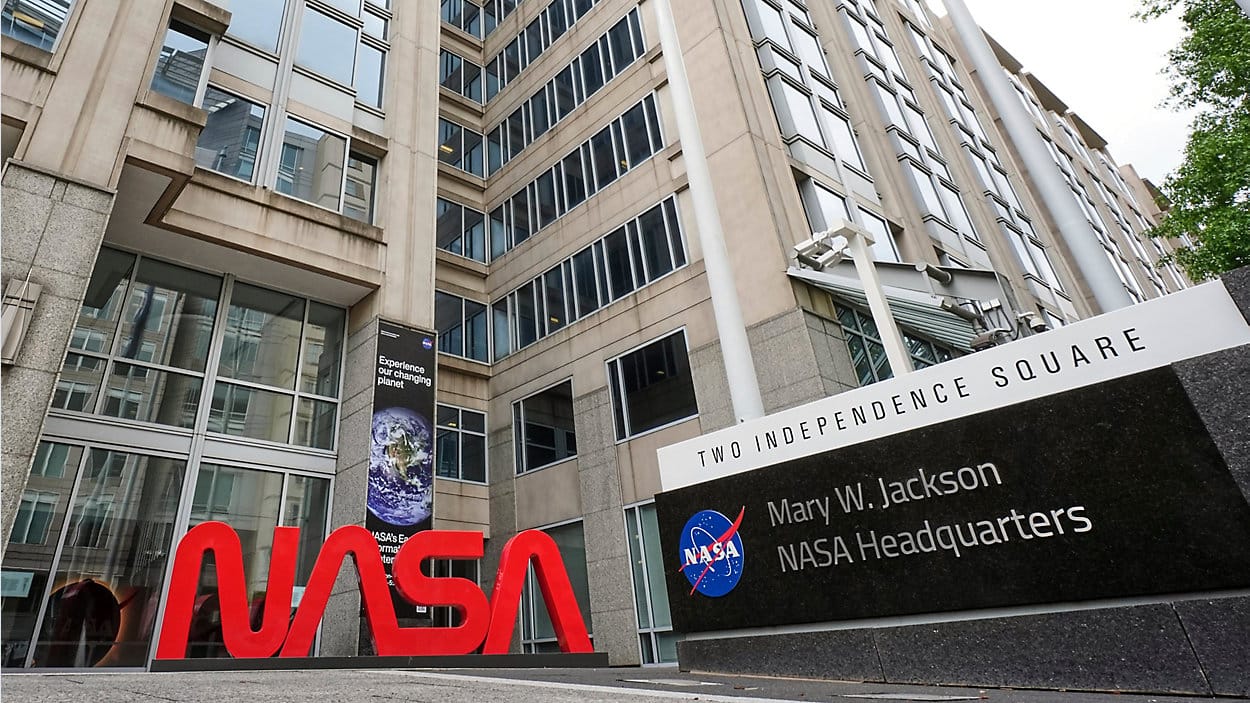 The Mary W. Jackson Building at Two Independence Square, NASA headquarters, Washington, D.C. NASA's "meatball" logo appears on the corner sign, and the "NASA" wordmark stands in front of the entrance.